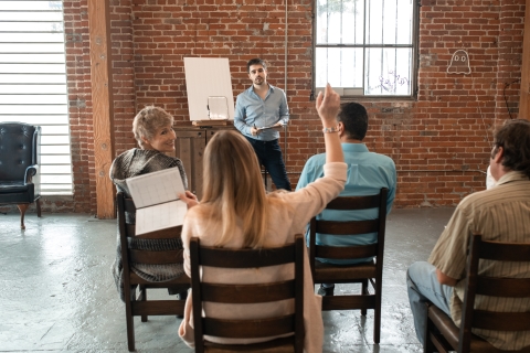 Man standing at the front of a room and woman raising her hand